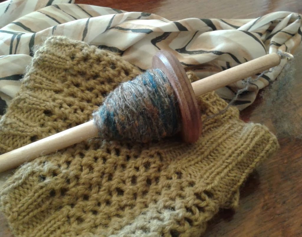 Spinning with carding waste: image of drop spindle with yarn spun from Ryeland wool and specks of carding waste