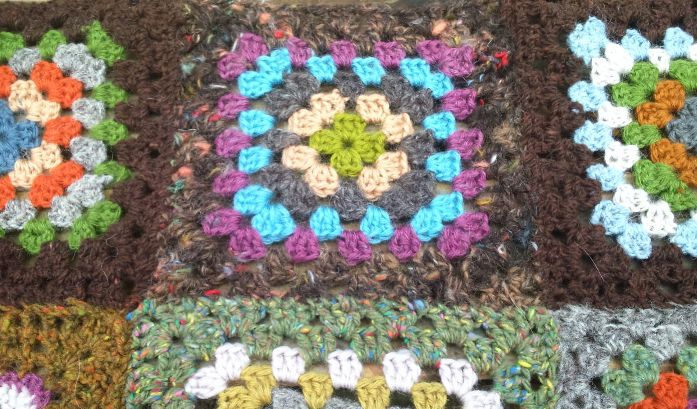 Image of part of an crocheted afghan blanket showing granny squares made from tweedy yarn, spun from trash batts