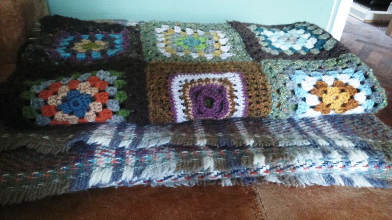 Image of afghan blanket folded on top of a chequered pure wool blanket on the sofa