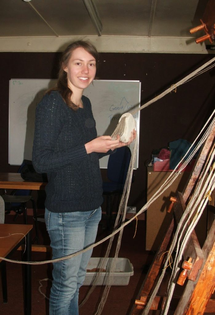 Preparing a warp-weighted loom: Image of tying on stone weights to warp threads