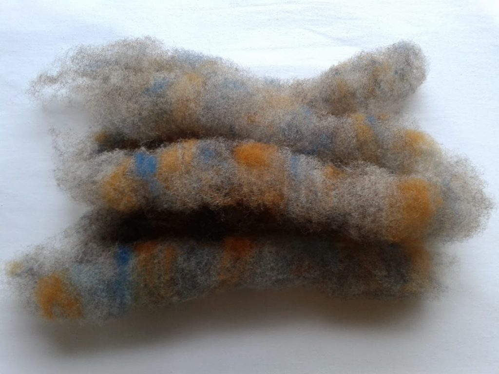 Spinning with carding waste: image of grey ryeland wool, including slithers of carding waste from dyed fleece, carded into rolags