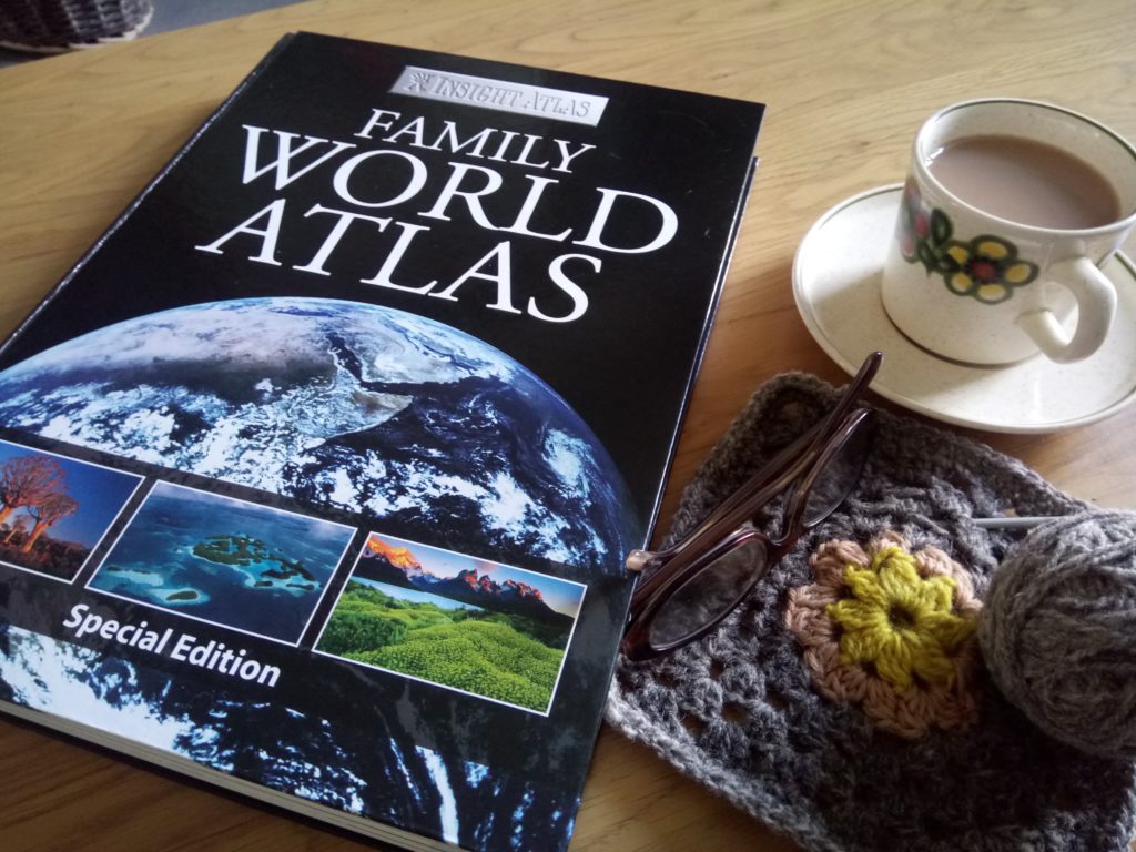 Homespun living: image of world atlas, crochet granny square made of pure wool, and a cup of tea to represent the fact that everything has to come from somewhere