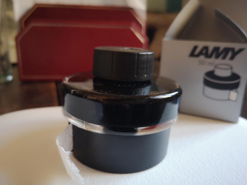 Bottle of Lamy ink, with plastic dispenser for blotting paper strip (with card packaging and a letter rack in the background)