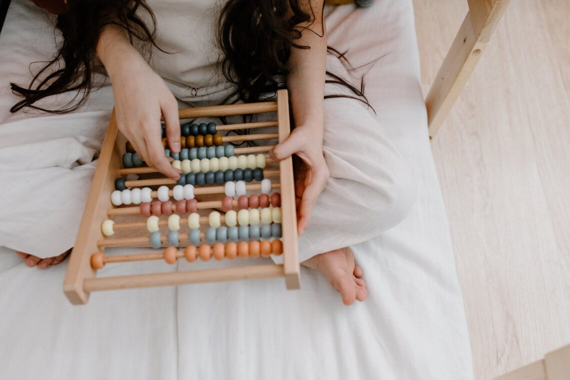 Numbers and carbon footprint calculators :a person using a wooden abacus toy while sitting on the bed