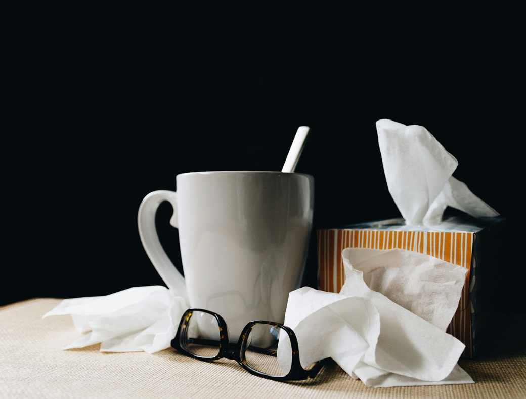 Contagion: cold cure: image of a box of tissues, a mug and spoon and pair of glasses, with a black background, Image by Kelly sikkema on Unsplash.